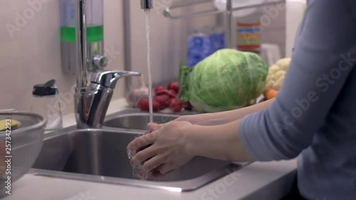 Female hands washing red apple in kitchen sink. Water is running and sparkling anding delicious fruit clean. Camera on slider