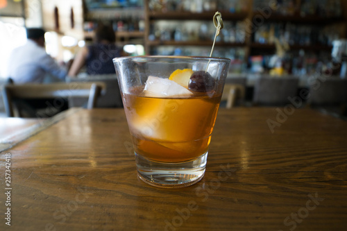 cocktail with orange and cherry garnish on a wooden table with couple in the background