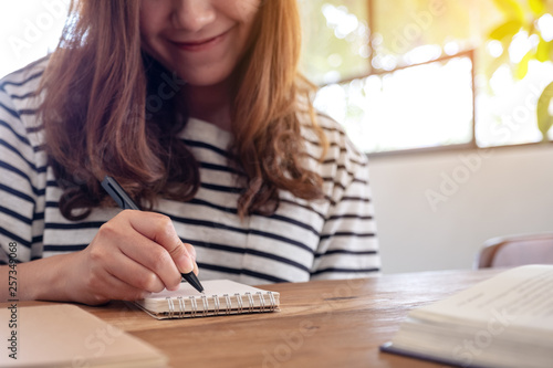 Closeup image of a woman writing on blank notebook and books on wooden table while learning