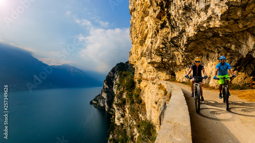 Cycling woman and man riding on bikes at sunrise mountains and Garda lake landscape. Couple cycling MTB enduro flow sentiero ponale trail track. Outdoor sport activity.