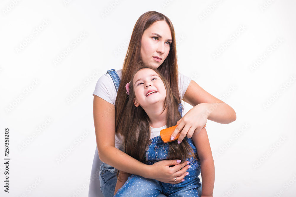 Family, motherhood and parent concept - mother combing her little daughter's hair isolated on white background Family, motherhood and parent concept - mother combing her little daughter's hair isolated on white background