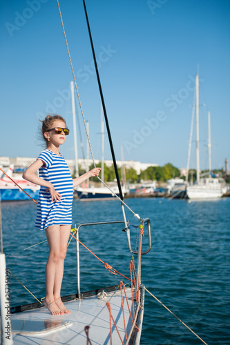 beautiful little girl in striped dress and sunglasses standing on yacht board during ocean cruise vacation travel in port in summer