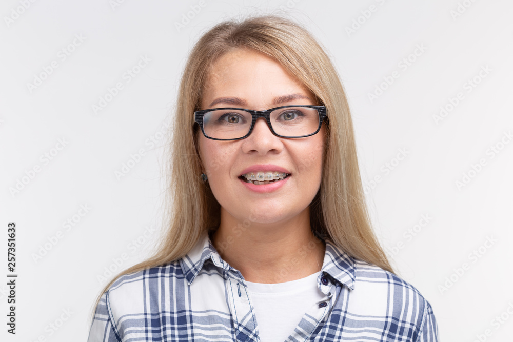 Teeth health, dentistry and bite correction - Happy smiling woman in glasses with braces on white background