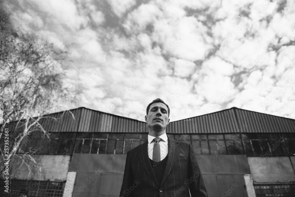 A man in a checkered suit poses on the street to advertise men's clothing. Black and white photo. Advertising menswear