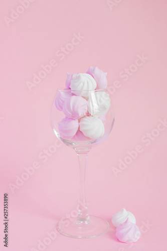 White and pink twisted meringues in a vine glass on pink background. French dessert prepared from whipped with sugar and baked egg whites. Greeting card with copy space
