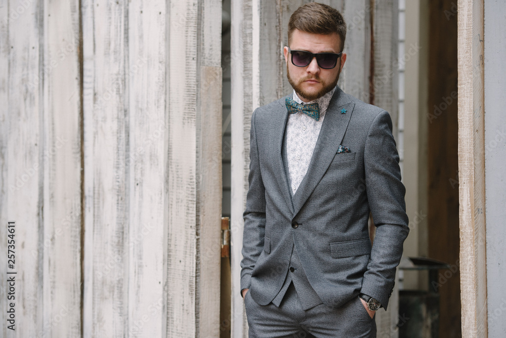 A man with a beard and sunglasses in a gray suit poses on the street to advertise men's clothing. Advertising menswear A man with a beard and sunglasses in a gray suit poses on the street to advertise men's clothing. Advertising menswear