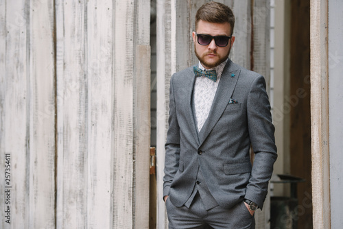 A man with a beard and sunglasses in a gray suit poses on the street to advertise men's clothing. Advertising menswear © Alexander
