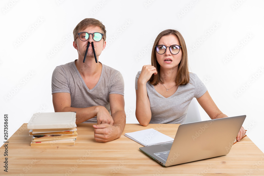 Education, fun and people concept - a couple of young people in glasses look like they are bored of learning homework and make a stupid jokes