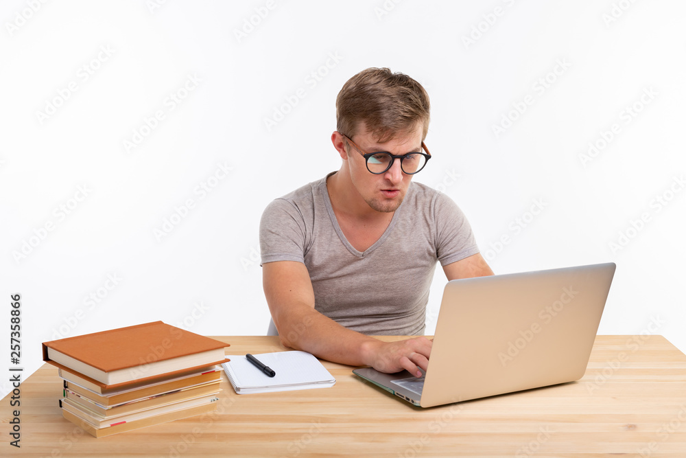 People and education concept - Puzzled student sitting at the wooden table with laptop People and education concept - Puzzled student sitting at the wooden table with laptop