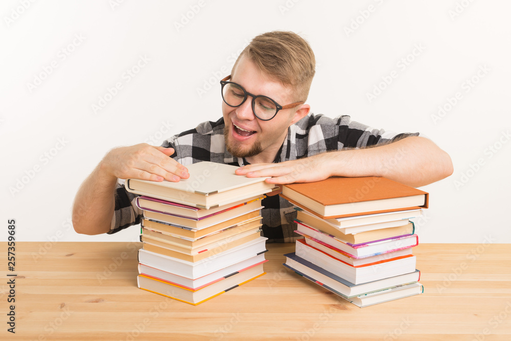 People, knowledge and education concept - smiling man sitting at the wooden table with books People, knowledge and education concept - smiling man sitting at the wooden table with books