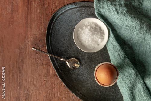 A boiled egg with coarse sea salt, shot from the top on a dark rustic wooden background with a place for text