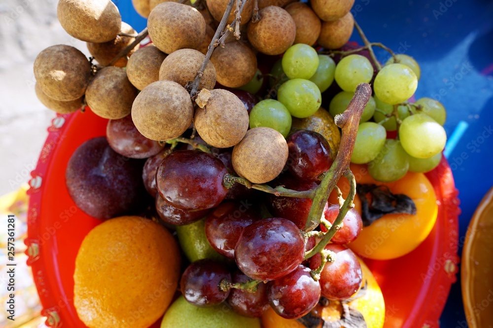 Top view of mixed fruit are fresh ripe red and green grape, longan, guava and persimmon in red plate, healthy food concept Top view of mixed fruit are fresh ripe red and green grape, longan, guava and persimmon in red plate, healthy food concept