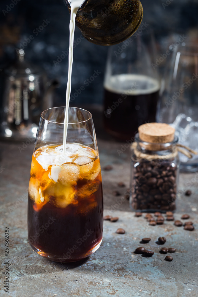 Ice coffee cold summer drink in a tall glass with pouring cream and coffee beans on a stone background. Ice coffee cold summer drink in a tall glass with pouring cream and coffee beans on a stone background.