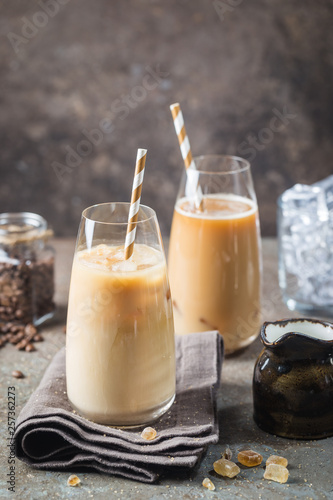 Ice coffee cold summer drink in a tall glass and coffee beans on a stone background.
