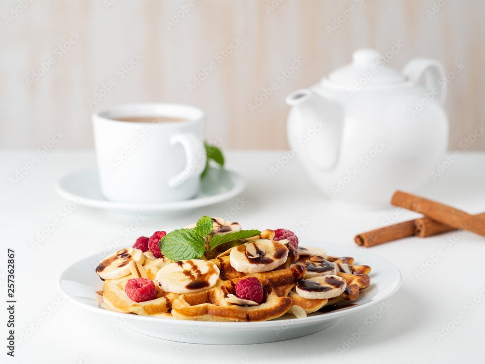 Belgian curd waffles with raspberries, banana, chocolate syrup. Breakfast with tea on white background, side view Belgian curd waffles with raspberries, banana, chocolate syrup. Breakfast with tea on white background, side view
