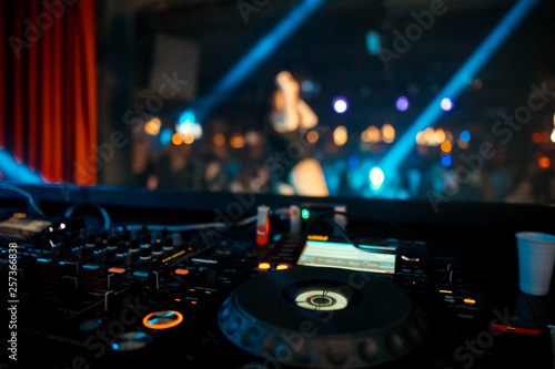 Dj mixes the track in the nightclub at party. On background of people dancing and a laser show