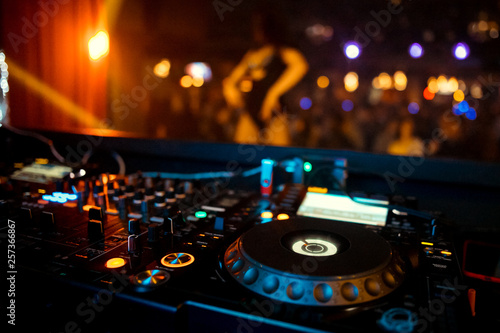 Dj mixes the track in the nightclub at party. On background of people dancing and a laser show