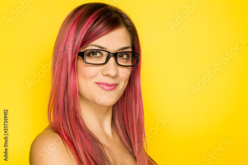 a happy woman with pink hair and glasses on yellow background