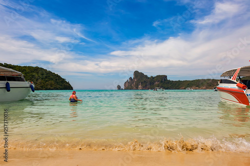 Overweight woman in a bathing suit comes into the sea for swimming. View on Phi Phi islands, sandy beach with waves and blue cloudy sky. Mountain on background