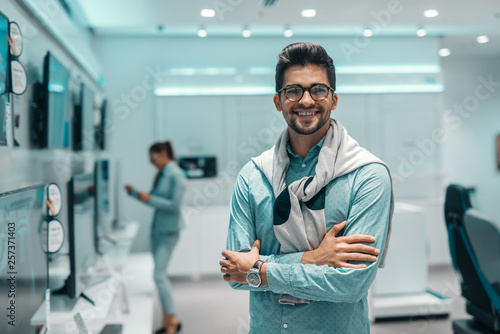 Smiling mixed race man dressed elegant standing in tech store and holding arms crossed.