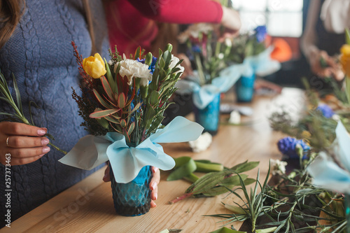 Fototapeta Naklejka Na Ścianę i Meble -  Women on the master-class on floristics. Young ladies making floral composition. Group of females with flowers indoor at the loft background. Decoration process.