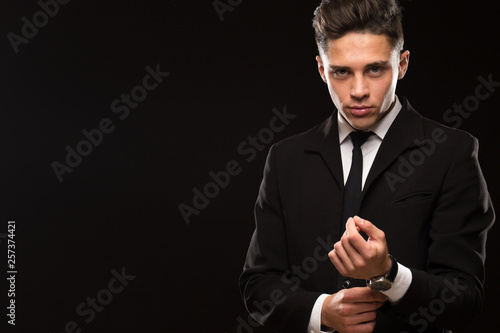 Εκτύπωση καμβά Attractive suited handsome businessman posing on black background adjusting his