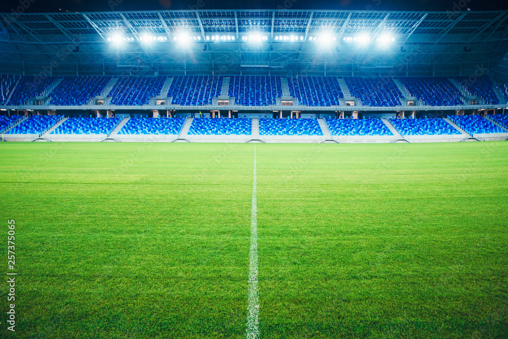 Modern Football Stadium in the evening. Soccer arena, background. Green grass, blue seats