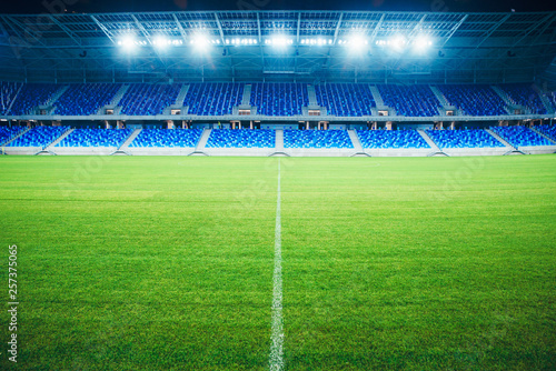 Modern Football Stadium in the evening. Soccer arena, background. Green grass, blue seats