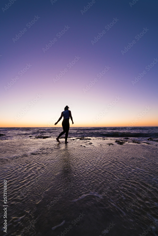 Silhouette of unidentifiable young woman performing a gymnastic / yoga pose at the beach during sunset.