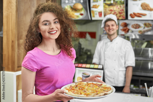 Pretty girl holding delicious pizza in pizzeria.
