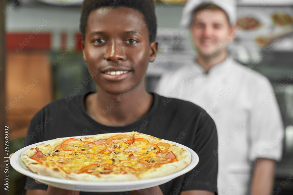 Smiling african holding italian pizza close up.