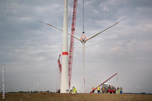 A construction crane lifts all three rotor blades of a wind turbine photo