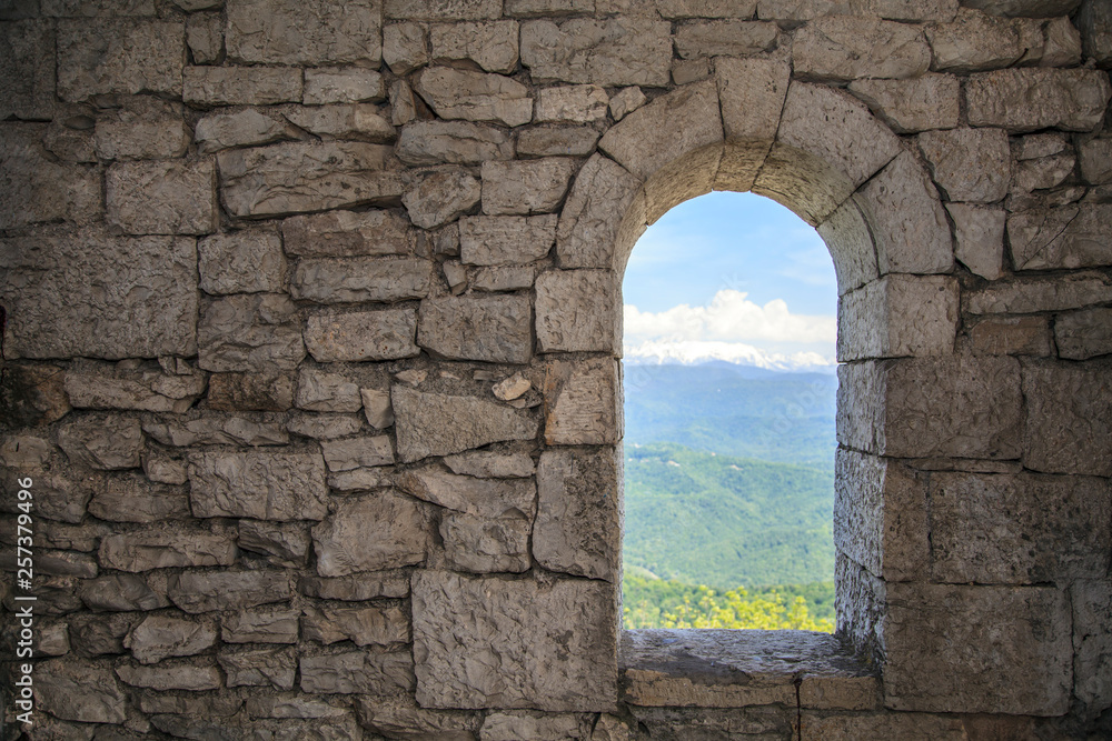 Stone war tower window with motion blurred bird and sea coast view with green tree hills