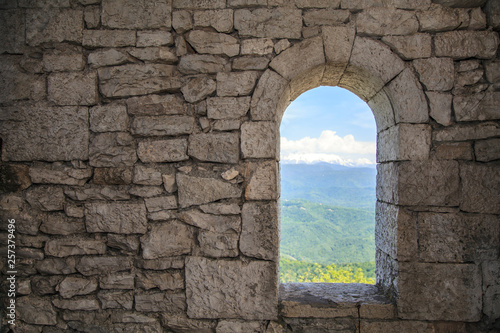 Stone war tower window with motion blurred bird and sea coast view with green tree hills