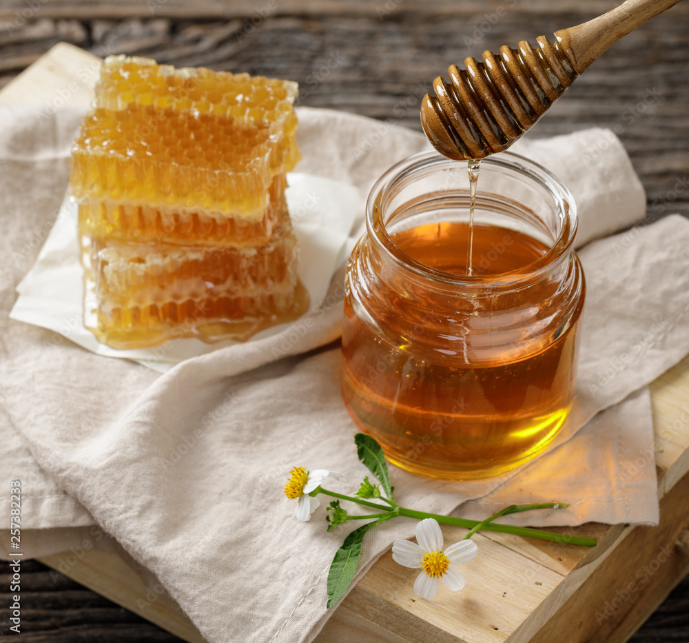 Honey bee in jar and honeycomb with honey dipper and flower on wooden table, bee products by organic natural ingredients concept Honey bee in jar and honeycomb with honey dipper and flower on wooden table, bee products by organic natural ingredients concept