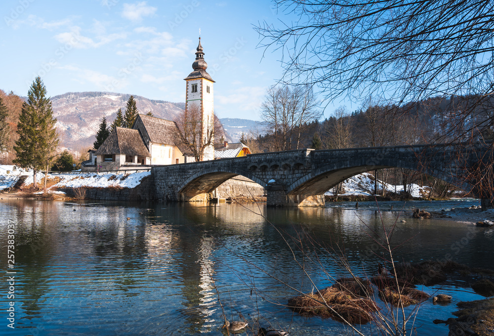 winter view of gothic church and stone bridge in ribcev laz, lake bhoinj, slovenia.