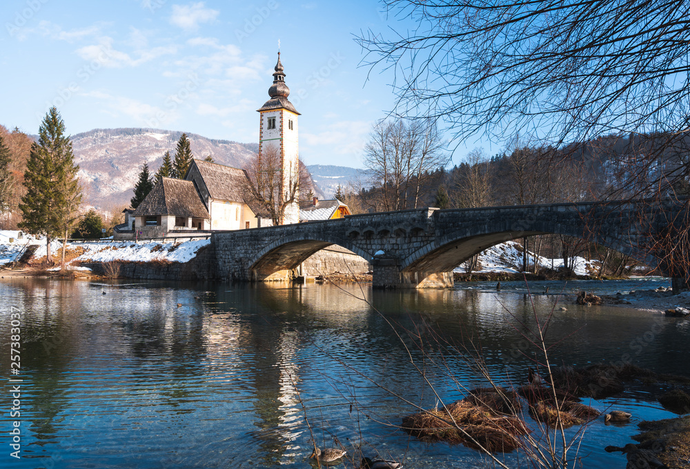Obraz premium winter view of gothic church and stone bridge in ribcev laz, lake bhoinj, slovenia.