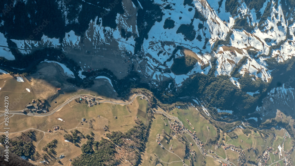 Stunning top down aerial views of mountain river valley high in the Swiss alps. The river winds its way through the valley floor surrounded by snow patches and fields.