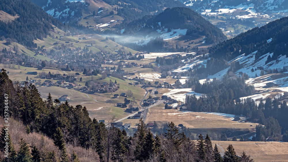 Stunning Aerial views over the a Swiss Alpine town and valley basin, surrounded by snow covered high mountain peaks and mountains.