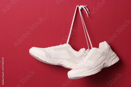 Fotografi Modern trendy sneakers hang on laces on a colored background