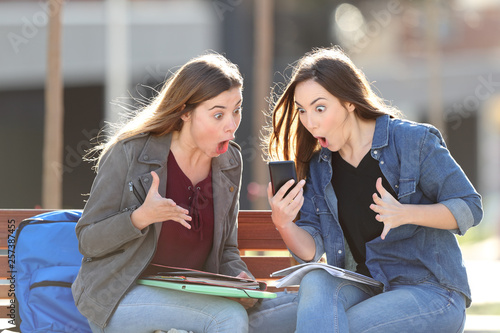 Two amazed students checking phone content in a park photo