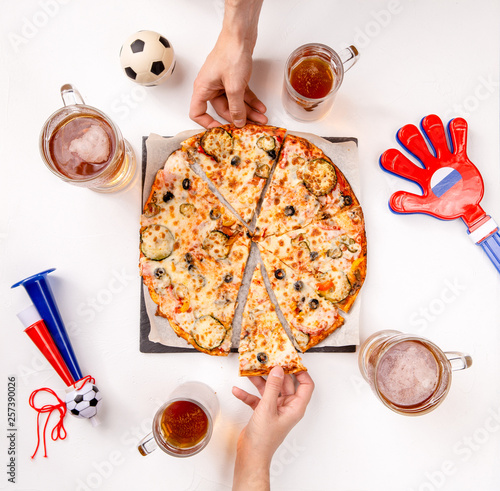 Photo top of hands of football fans with mugs of beer, pizza at white table photo