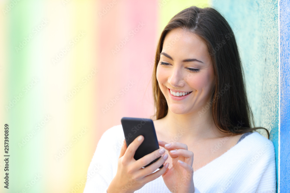 Happy woman using smart phone in a colorful wall Happy woman using smart phone in a colorful wall