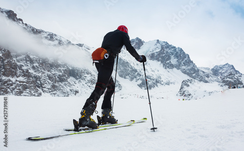 Mountaineer backcountry ski walking up along a snowy ridge with skis in the backpack. In background blue sky and shiny sun and Zebru, Ortler in South Tirol, Italy. Adventure winter extreme sport.