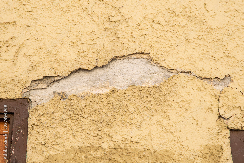 Obraz premium yellow plaster on a house wall which has a crack and crumbles off as a background