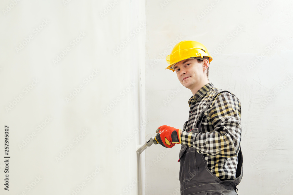 Young male builder and repairman in a yellow helmet plastering the wall with a spatula and plaster. Young male builder and repairman in a yellow helmet plastering the wall with a spatula and plaster.