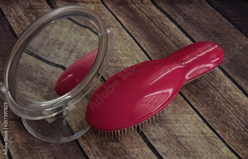 pink hairbrush and round table mirror on a wooden background