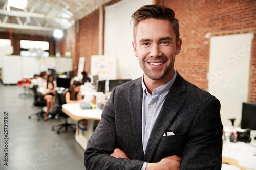 Portrait Of Businessman In Modern Open Plan Office With Business Team Working In Background