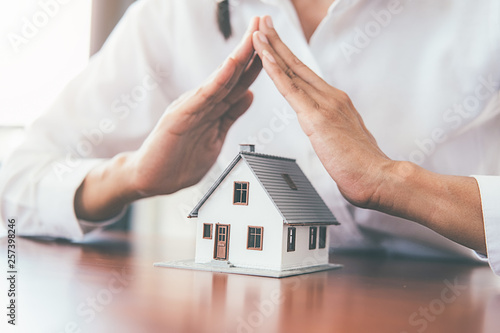 Saving money for house and real estate. Woman hand protecting on stack coins and house model on table.