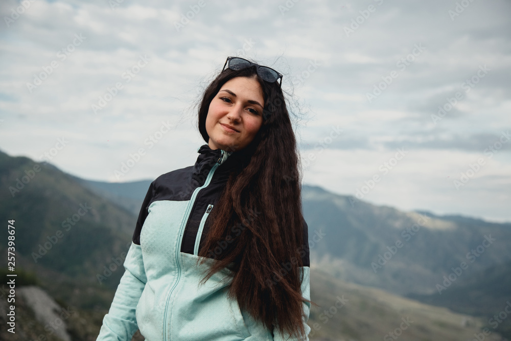 Naklejka premium Girl smiling in a turquoise jacket sitting on the mountain. Enjoys the beautiful view around.